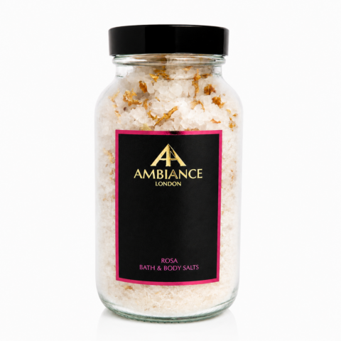 A clear jar filled with bath salts, featuring a black label with gold "Ancienne Ambiance London," logo and a pink border. The label also says "ROSA BATH & BODY SALTS."