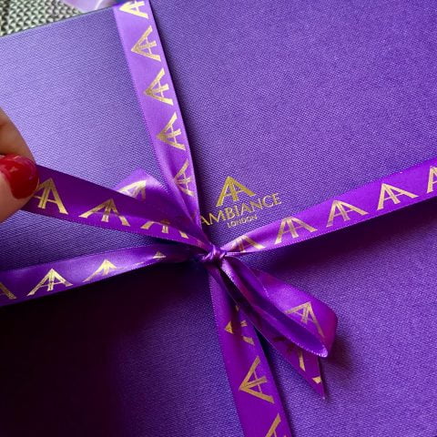 An iconic Ambiance London purple gift box, tied up with signature purple satin and gold foil ribbon, is about to be unwrapped.