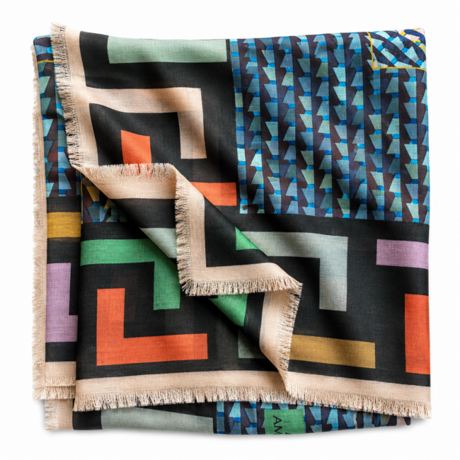 Folded scarf with colourful geometric patterns on a black background, featuring bold stripes, triangles, and fringe edges. Vibrant and eclectic design.