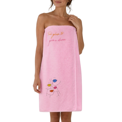 A woman is wrapped in a pink towelling wrap dress that says "Too glam to give a damn," featuring colourful abstract faces. The mood is playful and confident.