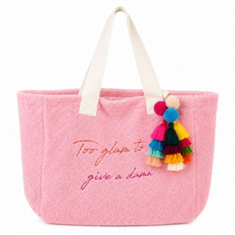 Bright pink towelling tote bag with white cotton handles, featuring the phrase "Too glam to give a damn" embroidered in rainbow colours. Adorned with colourful tassels.