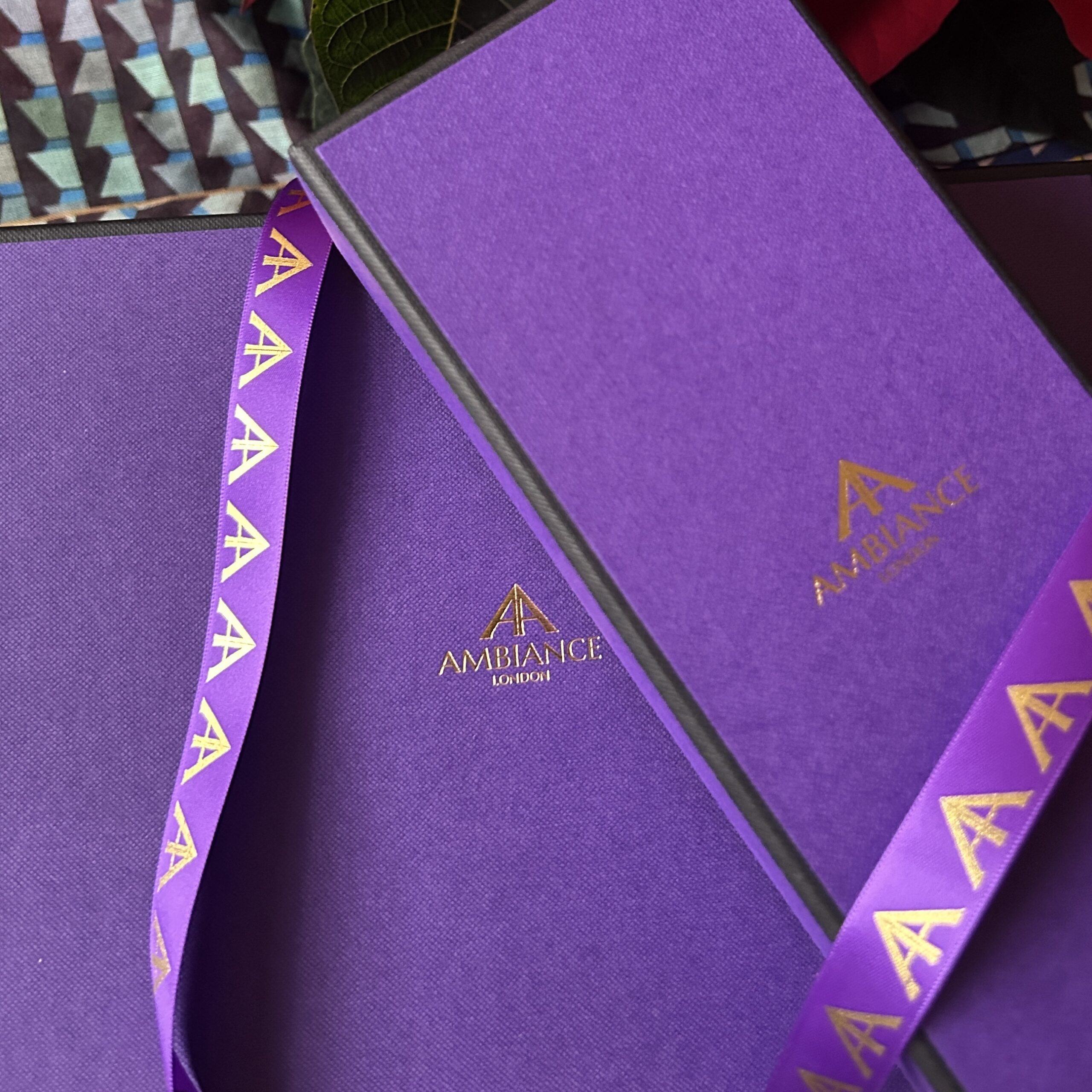 Two purple gift boxes with "Ancienne Ambiance London" logo embossed in gold. Matching ribbon with gold logo wraps around, conveying luxury and elegance.