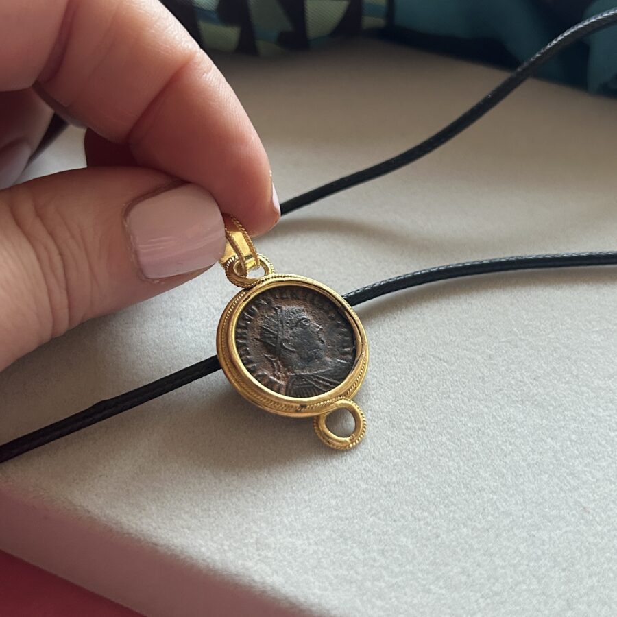 Close-up of a hand holding an Etruscan revival style gold pendant with an ancient Roman Constantius Maximianus bronze coin.