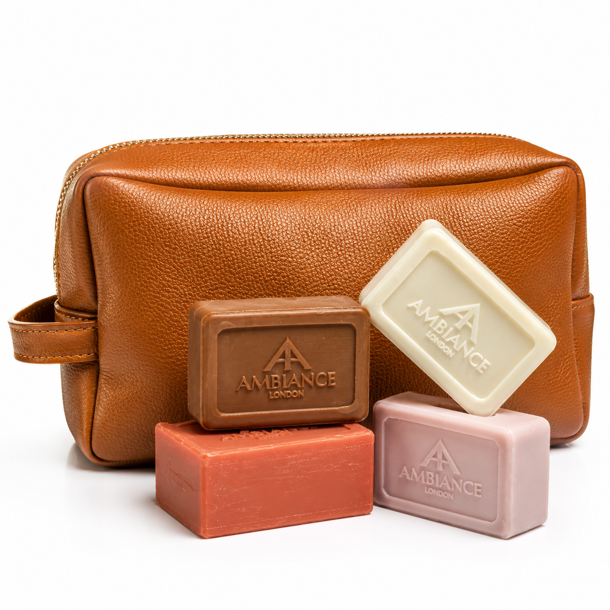 Brown leather toiletry bag with a handle, set behind four soap bars in white, brown, pink, and red with "Ancienne Ambiance London" branding. Clean, elegant vibe.