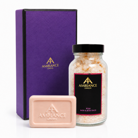 Purple box, glass jar of pink rose bath salts, and embossed rose soap bar elegantly displayed. Ancienne Ambiance London branding; luxurious and soothing tone.