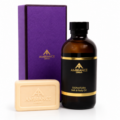 Elegant bath and body set featuring a purple box, amber bottle with gold accents labeled "Signatura Bath & Body Oil," and neroli orange blossom soap bar.