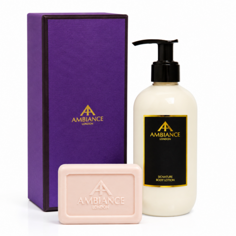 Luxury bath set with a purple box, cream-coloured bottle labeled "Ancienne Ambiance London" and "Signature Body Lotion," and a pink bar soap. Elegant and refined.
