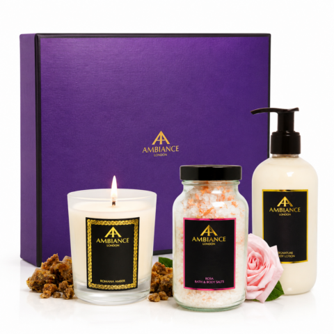 A luxurious gift set with a purple box containing a lit candle, bath salts, body lotion, and a pink rose. The vibe is calming and elegant.