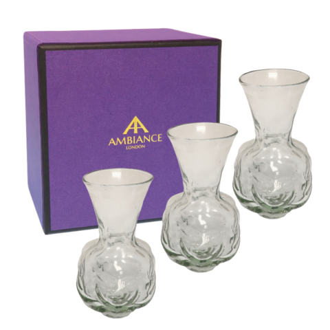 Three La Soufflerie clear glass face vases are positioned in front of a purple box with a gold Ancienne Ambiance London logo. The scene conveys elegance and luxury.
