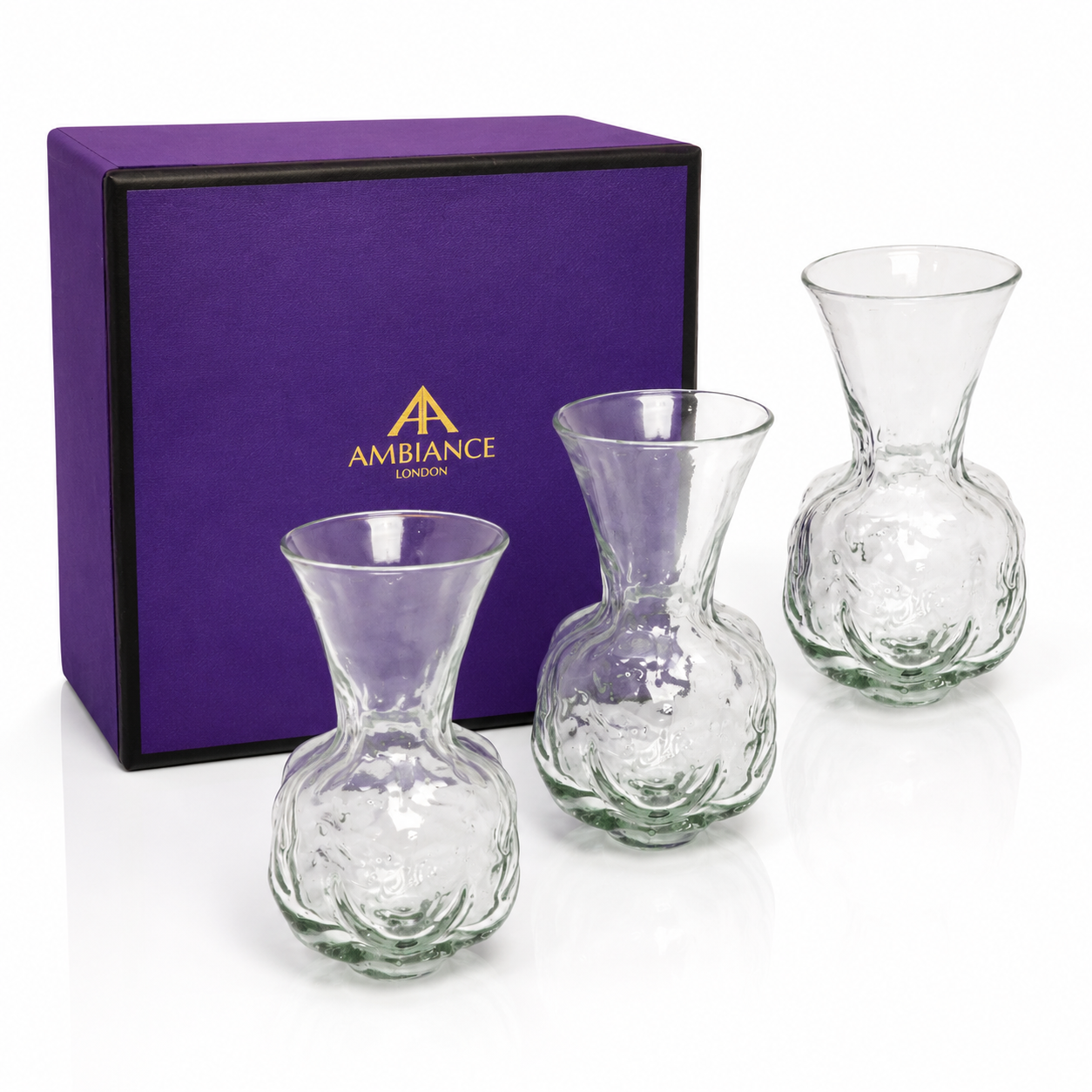 Three elegant glass bud vases with wide openings are displayed in front of a purple gift box labeled "Ancienne Ambiance London," conveying a sense of luxury.