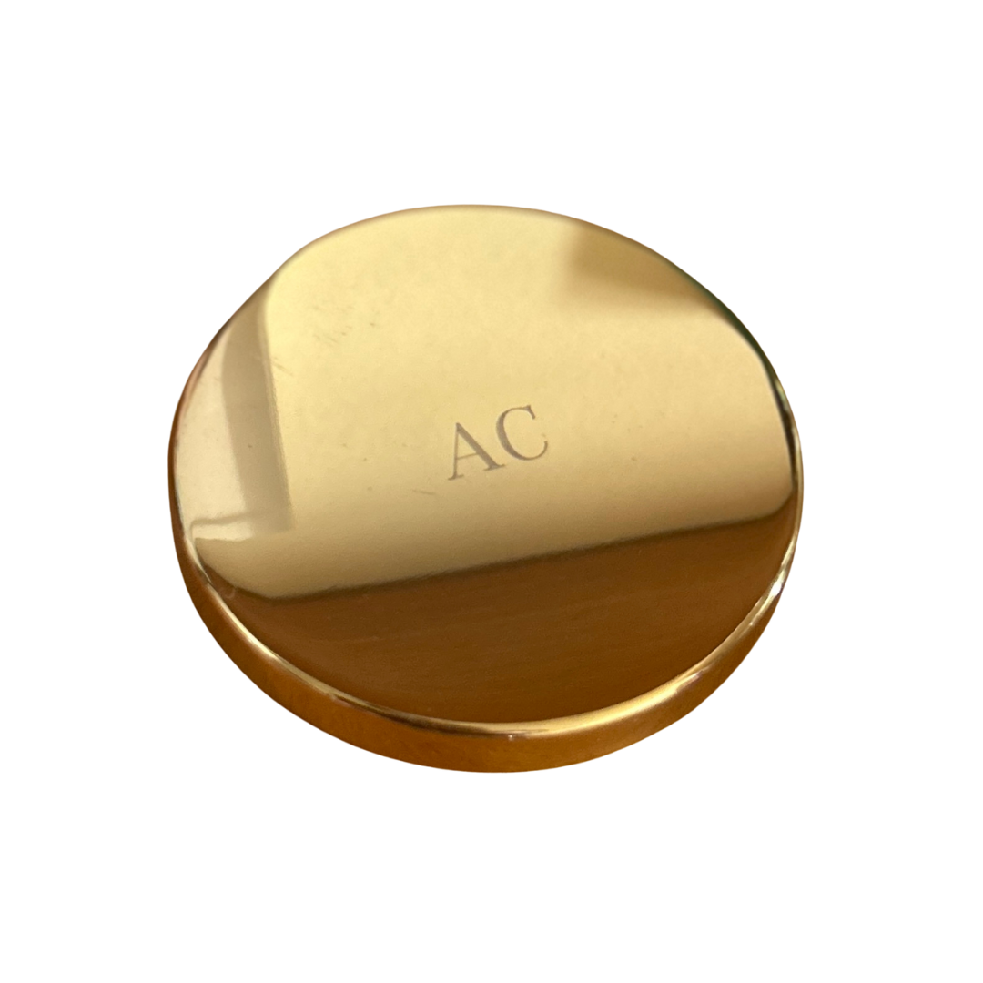 A gold candle lid with a monogram engraved with someone's initials.