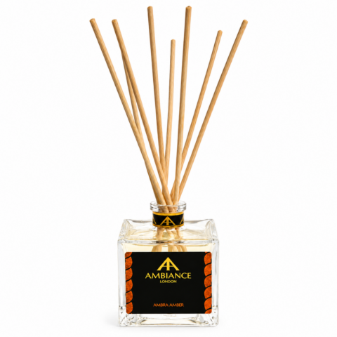 Clear glass diffuser with wooden reeds, featuring a black and gold label reading "Ambiance London, Ambra Amber." Elegant and calming design.