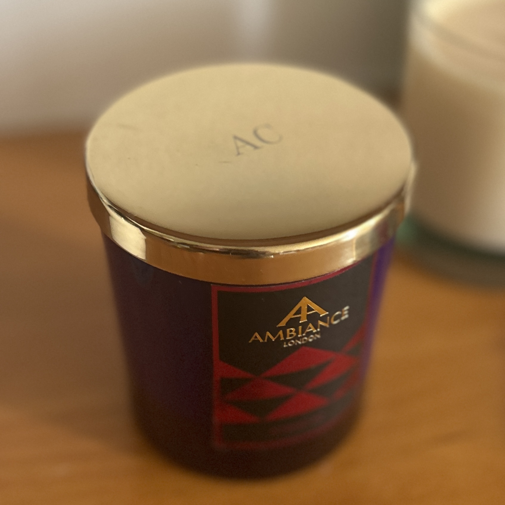 A gold candle lid with a monogram engraved with someone's initials on an Ancienne Ambiance London candle.