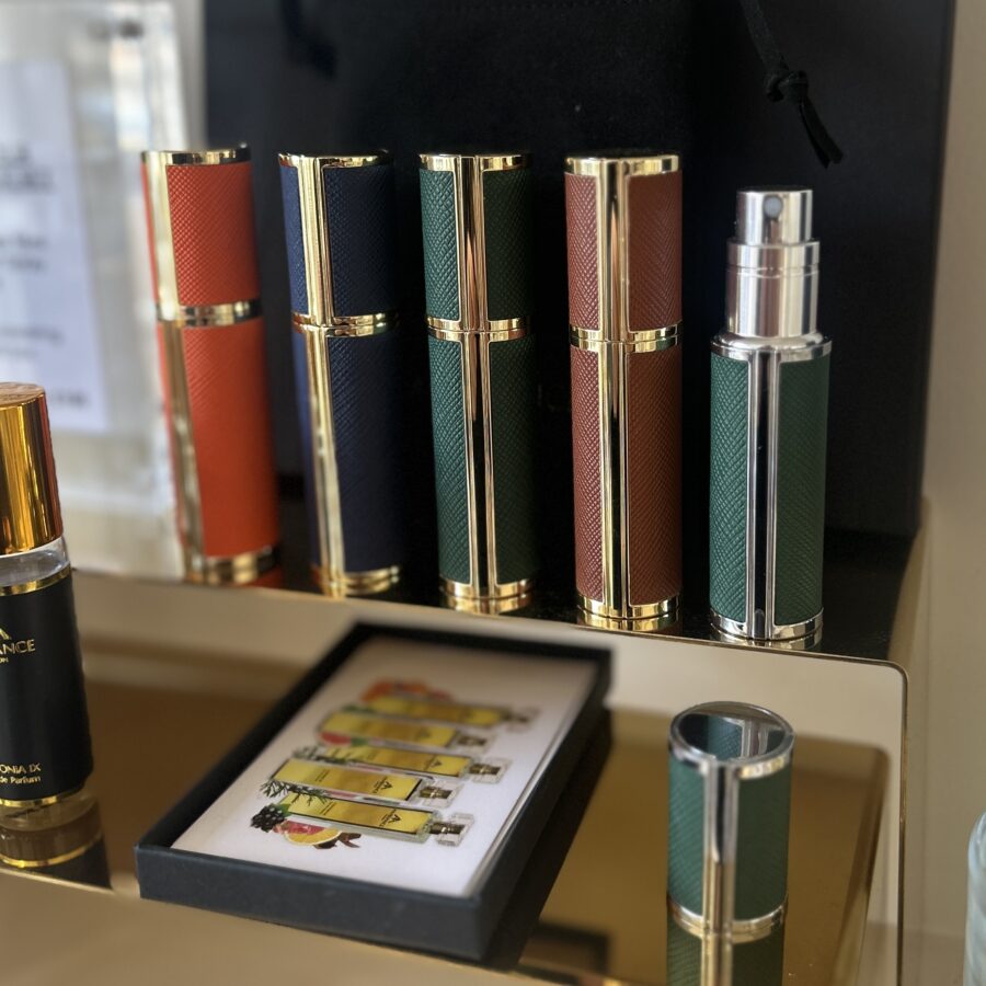 Five refillable travel perfume atomisers on a golden shelf.