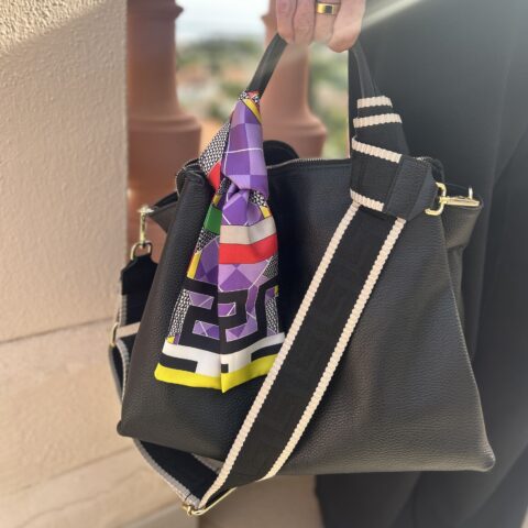 A multicoloured silk twilly scarf on the handle of a black leather handbag.