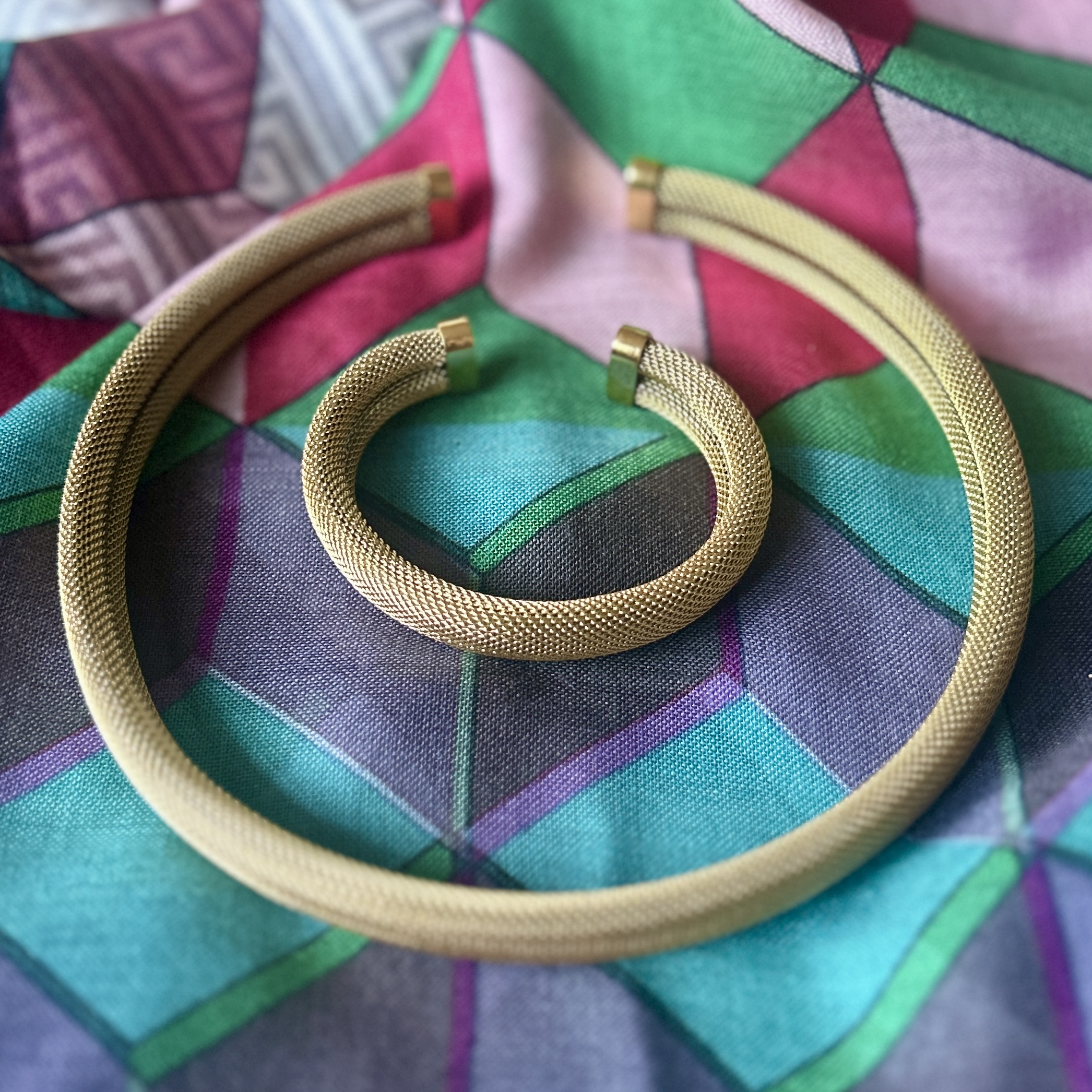 A gold torque necklace and bangle bracelet resting on a colourful scarf, showcasing style elegance.