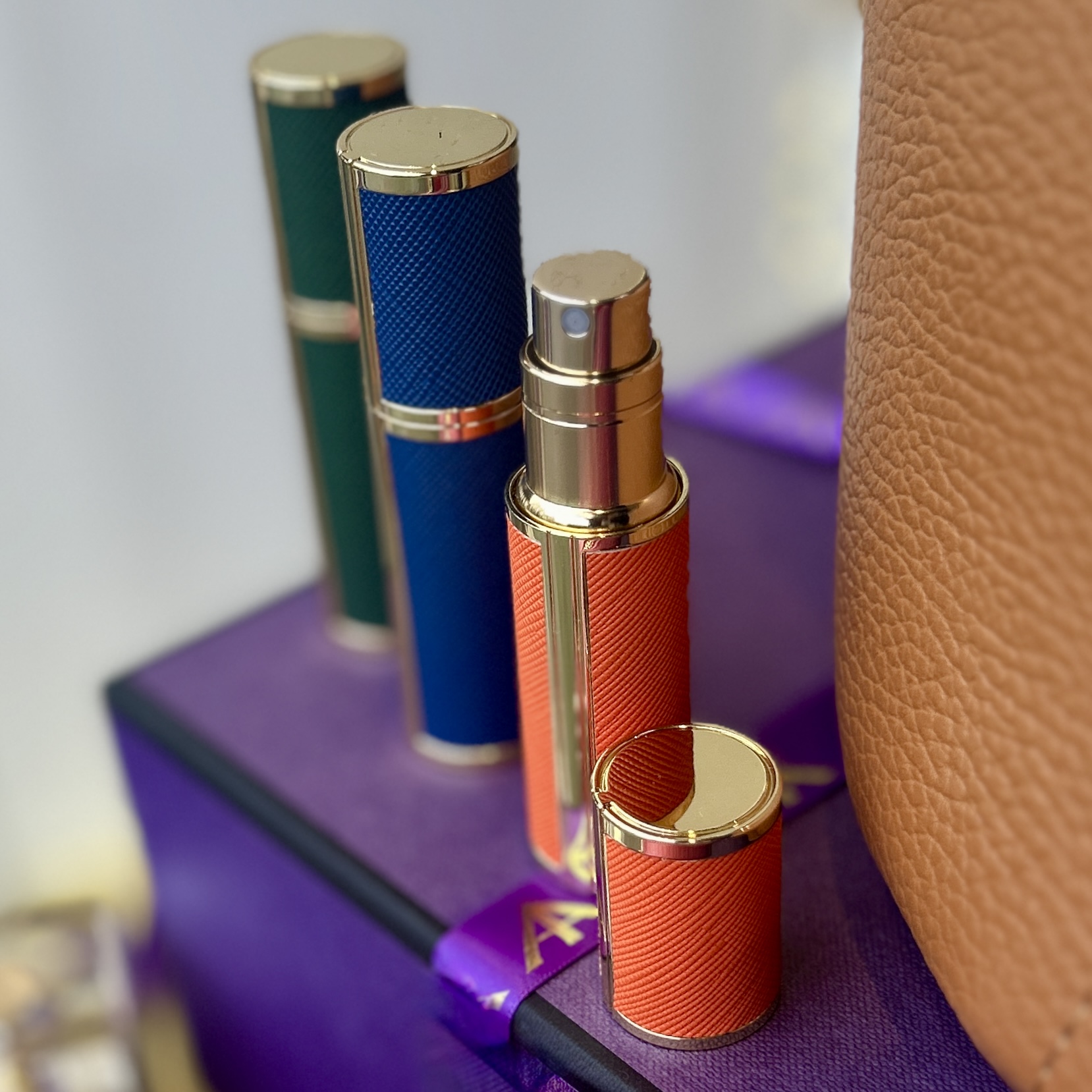 Three colourful travel perfume atomisers sit on a purple box.
