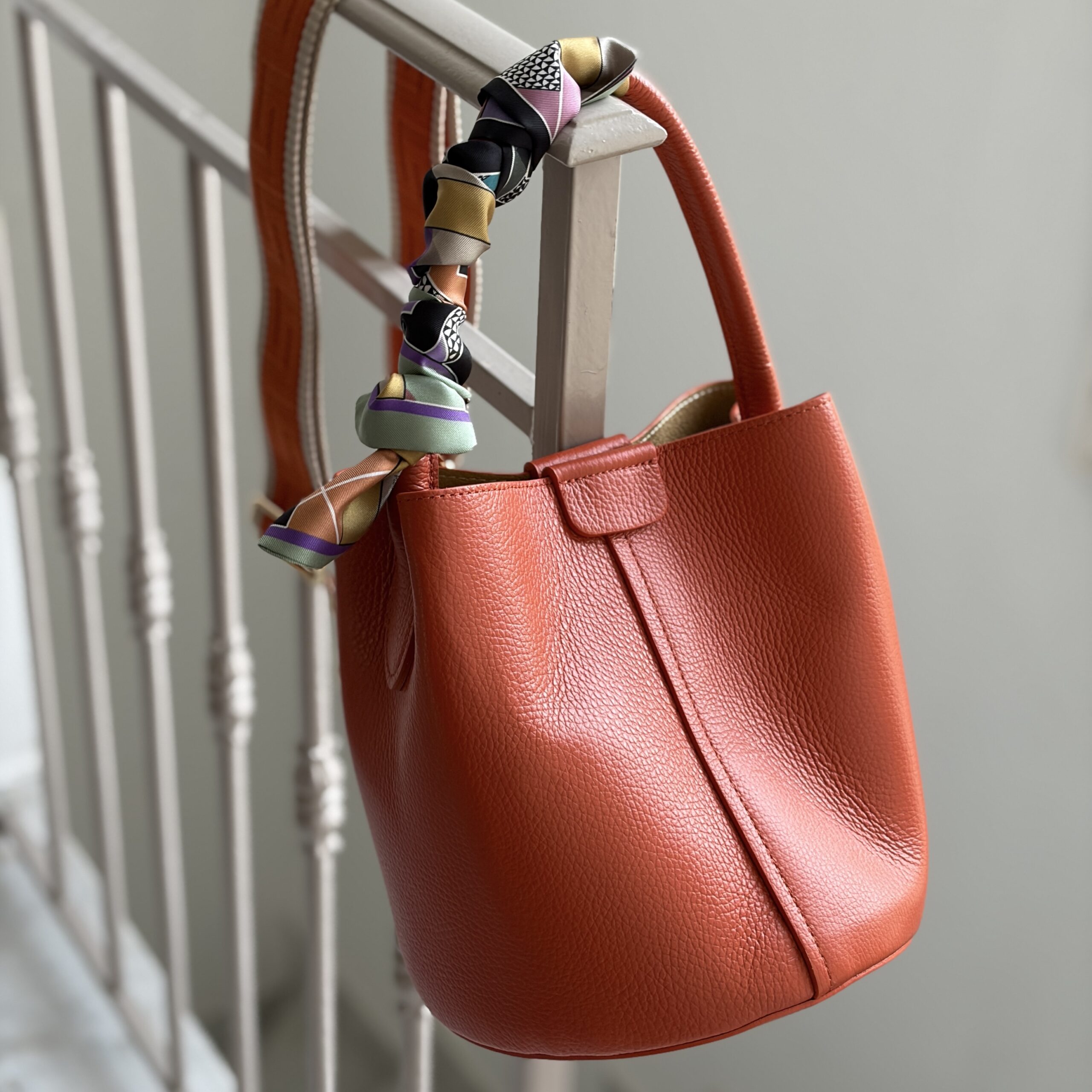 Greek key print twilly silk scarf on a orange leather bucket bag.
