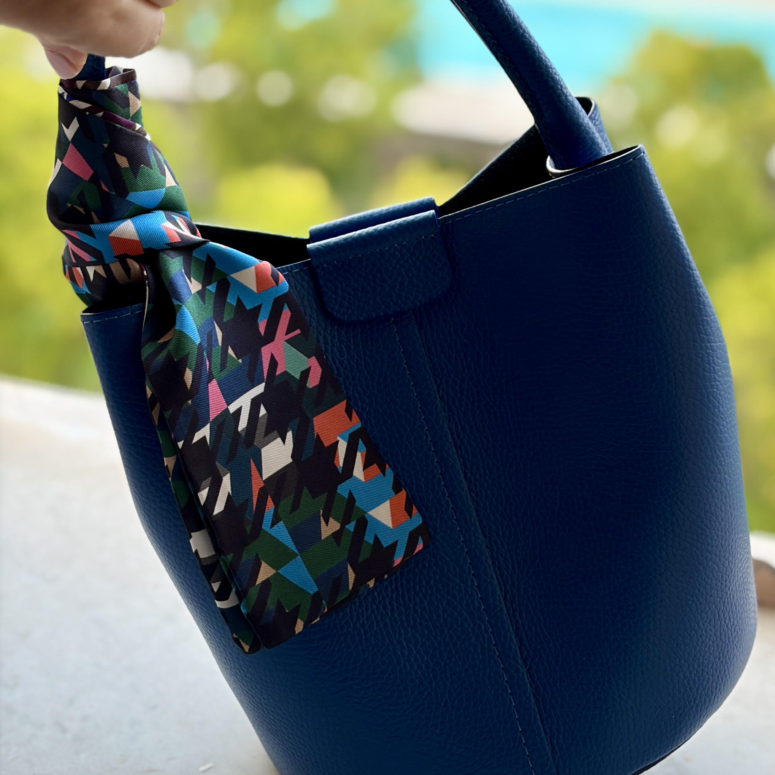 Artemis houndstooth pring twilly silk scarf on a blue leather bucket bag.