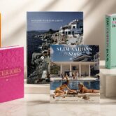 Six stylish coffee table books displayed on a marble surface. Covers feature vibrant visuals of flowers, fashion, interiors, and scenic photography.