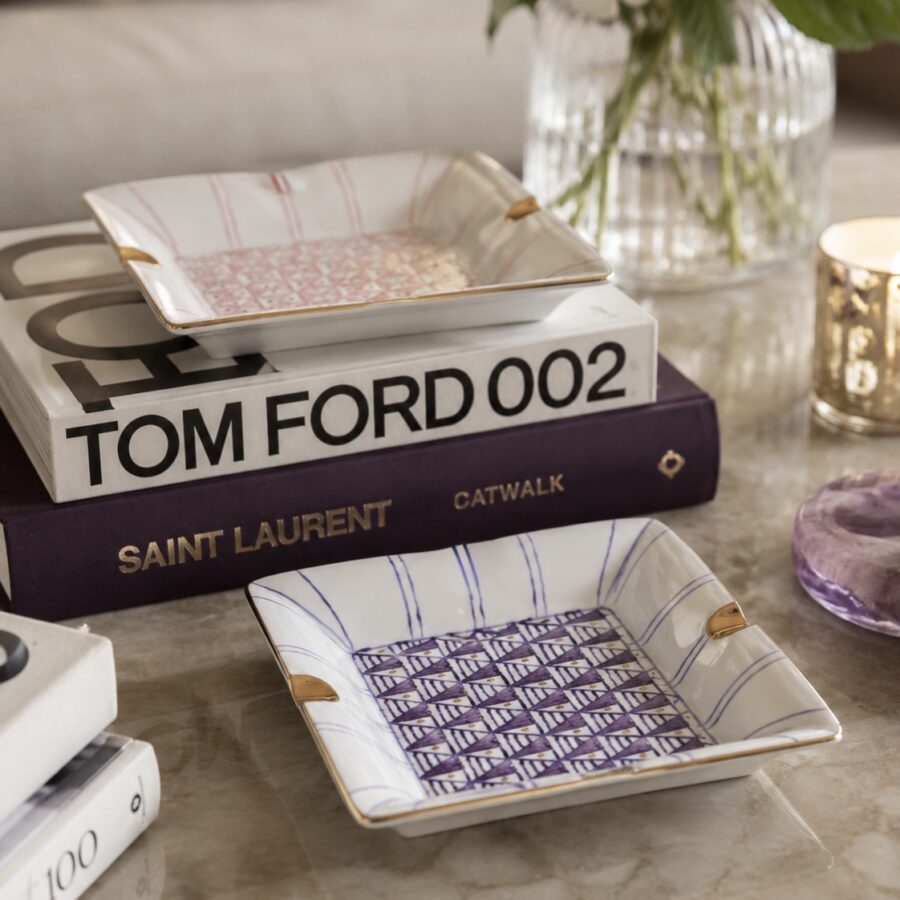 Two decorative porcelain vide poche trays with geometric patterns sit atop fashion books titled "Tom Ford 002" and "Saint Laurent Catwalk," creating a chic, elegant vibe.