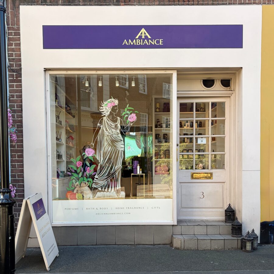 Front of "Ancienne Ambiance London" store in Chelsea featuring a purple signage and elegant window display with a classical statue illustration and pink flowers, creating a welcoming, artistic vibe.