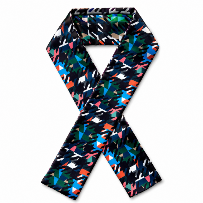 A colourful silk twilly scarf with an abstract geometric pattern in red, blue, green, and white on a dark background is folded in an X shape. Bright and stylish.