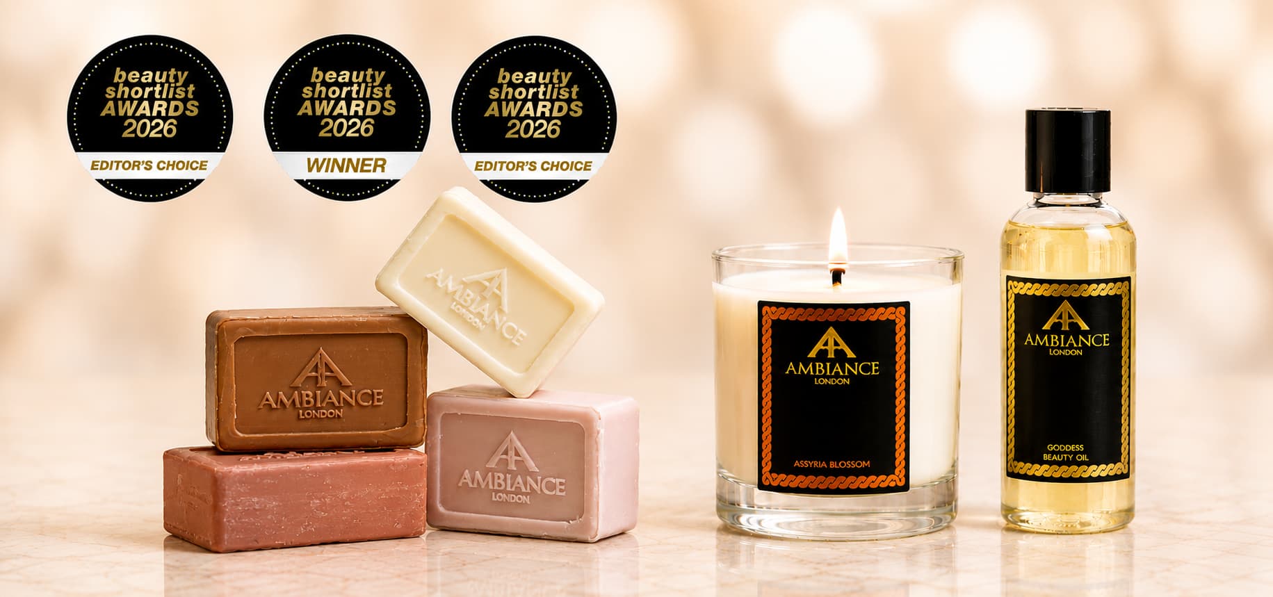 Ancienne Ambiance London products displayed elegantly on a marble surface, featuring soap bars, a lit assyria blossom candle and a bottle of goddess beauty oil. Three beauty awards badges are shown above.