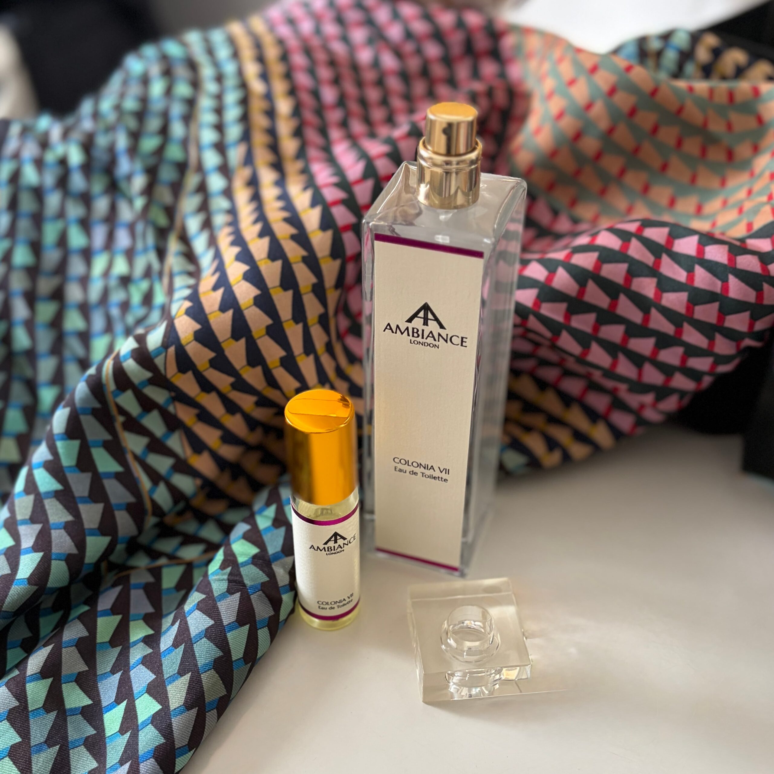 Elegant scene of Ancienne Ambiance London Colonia VII eau de toilette perfume bottles on a colourful, patterned silk scarf.