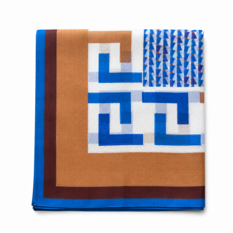 A folded cotton silk scarf with geometric patterns in blue, brown, and white. It features a border with blue edges and a central grid design.