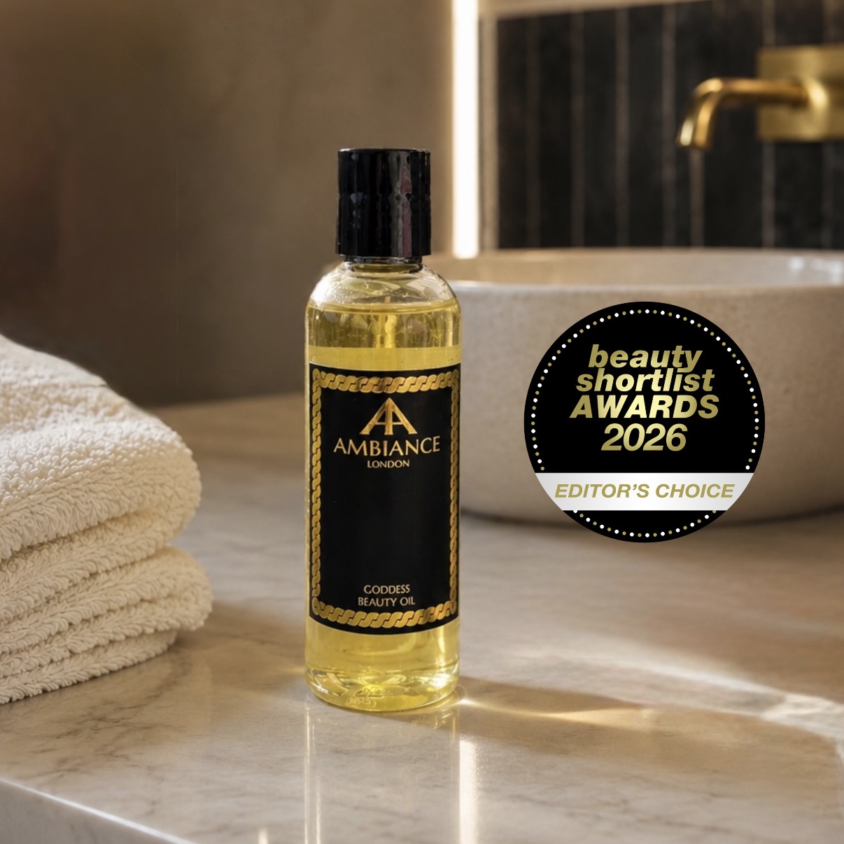 A bottle of Ancienne Ambiance London Goddess Beauty Oil on a marble bathroom counter beside folded towels. Features an award badge for "Editor's Choice 2026."