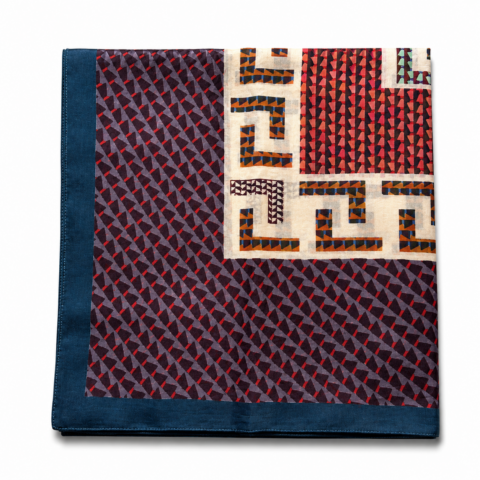 A folded scarf features blue, red, and black geometric patterns with a navy border. The intricate designs convey a modern and vibrant feel.