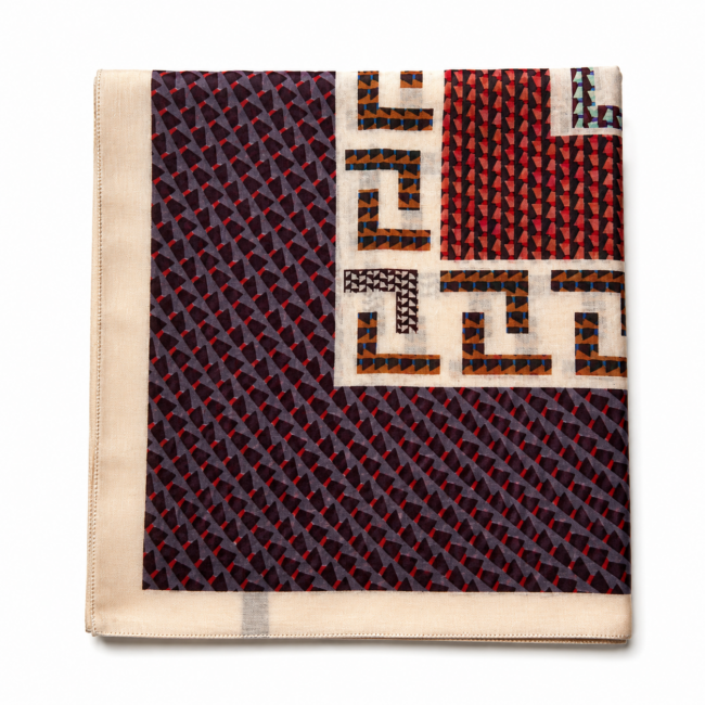Folded cotton scarf with geometric patterns: navy with red diagonal lines and beige with multicoloured Greek key design. Modern and stylish aesthetic.