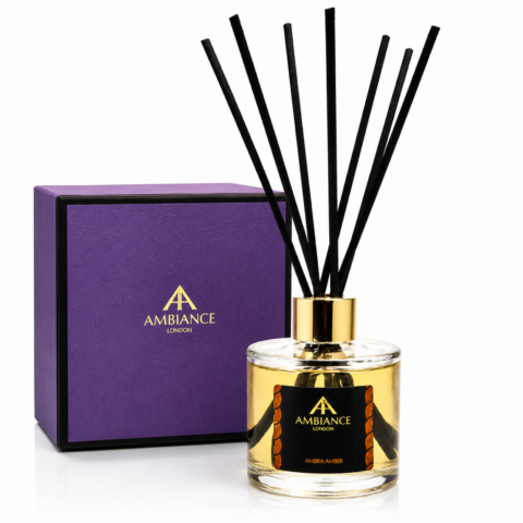 Reed diffuser with black sticks in a clear glass bottle labeled "Ambra Amber." Accompanying it is a purple box marked "Ancienne Ambiance London." Classy and elegant.