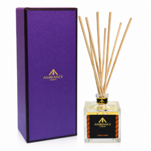 A purple box with "Ancienne Ambiance London" branding stands beside a square glass Ambra Amber diffuser with natural reeds. The tone is elegant and sophisticated.