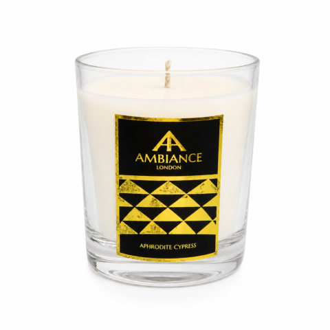 A scented candle in a clear glass holder with a black and gold label. The label reads "Ambiance London, Aphrodite Cypress" in elegant lettering.