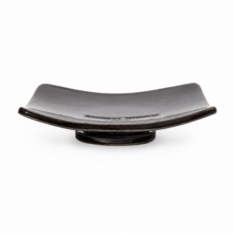 A sleek, rectangular black ceramic soap dish with slightly upturned edges sits on a small pedestal base, against a white background.