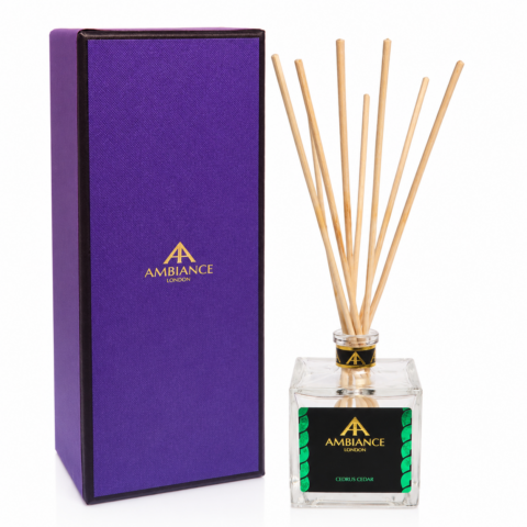 Purple box with gold "Ancienne Ambiance London" logo next to a glass cedar fragrance diffuser with wooden reeds and a black label, creating a luxurious feel.