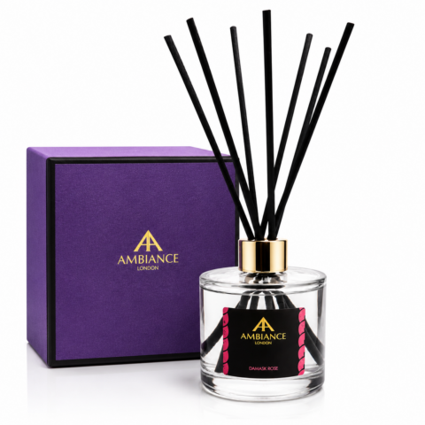 A luxurious fragrance diffuser with black reeds in a clear bottle labeled "Ancienne Ambiance London, Damask Rose." It sits beside a purple box with gold lettering.