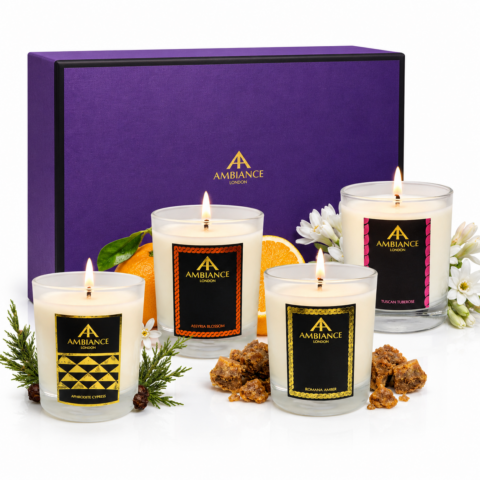 Four lit Ancienne Ambiance London scented candles with elegant labels, surrounded by orange slices, white flowers, and herbs, in front of a luxurious purple gift box.