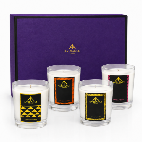 Four elegant candles in glass holders with colourful Ancienne Ambiance London labels are arranged in front of a luxurious purple box with gold detailing.