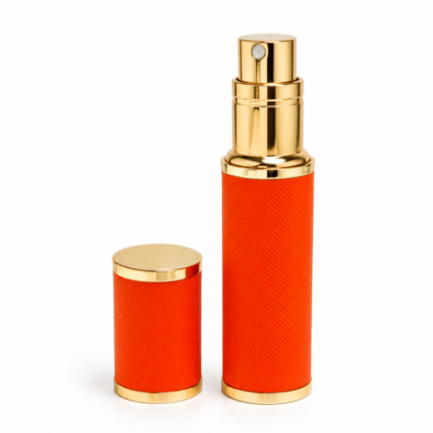 Travel perfume atomiser with orange and gold design, and a spray top; matching cap beside it. Elegant, luxurious, and modern.