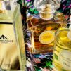 Three elegant perfume bottles—Ancienne Ambiance Colonia, L'Heure Bleue, and Dior—are displayed on a vibrant, multicoloured fabric, conveying luxury and sophistication.