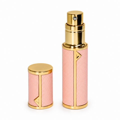 A pink, textured travel perfume atomiser with gold accents is shown. The cap is also gold-toned and rests beside the bottle, conveying elegance and luxury.