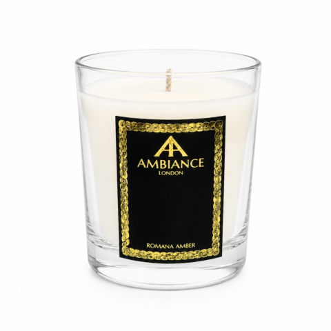 A white candle in a glass jar features a black label with gold Ancienne Ambiance London logo and the text "ROMANA AMBER," evoking elegance.