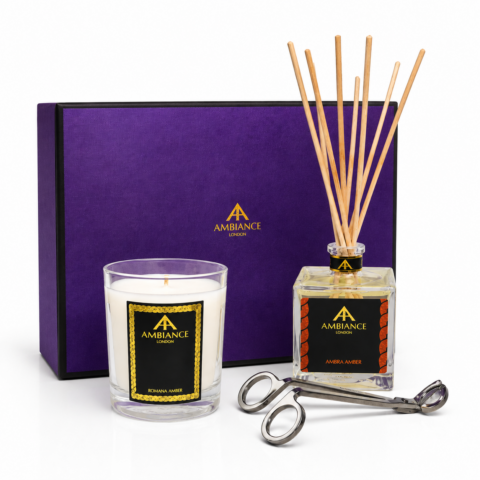 Purple gift box with "Ancienne Ambiance London" logo, a Romana Amber candle beside it, a square Ambra Amber diffuser with reeds, and silver candle wick trimmer. Elegant and calming.