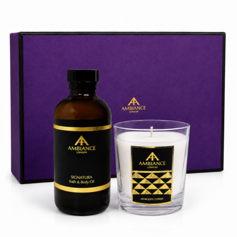 A purple gift box with "Ancienne Ambiance London" branding, featuring an amber signatura bath oil bottle and a white aphrodite cypress scented candle in glass, conveying luxury and relaxation.