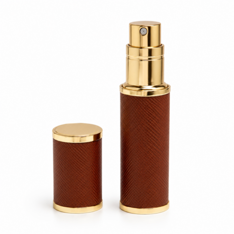 A tan brown and gold travel perfume atomizer with a textured surface is shown. The cap is removed, revealing a golden spray nozzle, conveying elegance.