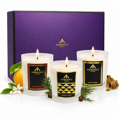 Three lit candles labeled "Ancienne Ambiance London" are displayed in front of a purple gift box. Scents include Assyria Blossom, Aphrodite Cypress, and Romana Amber.