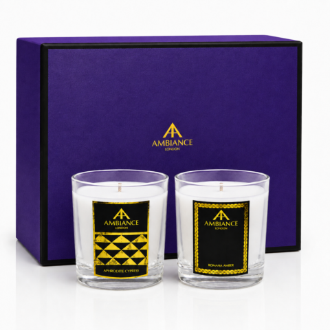 Purple gift box with "Ancienne Ambiance London" branding contains two scented candles in glass jars. Labels read "Aphrodite Cypress" and "Romana Amber."